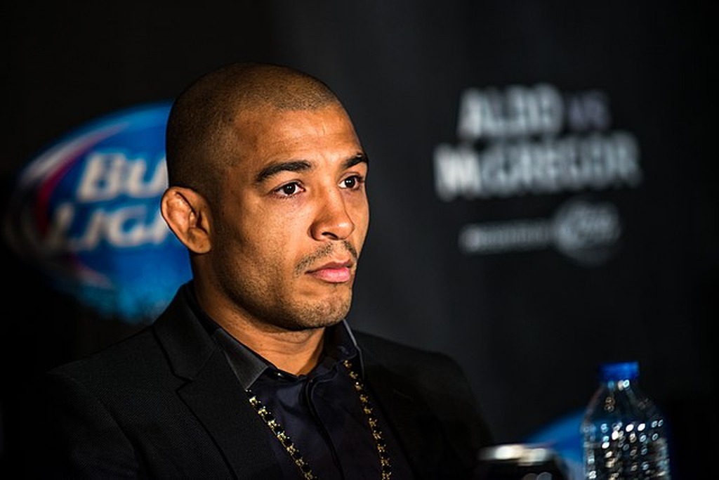 Lutador de UFC José alfo, vestindo roupa inteiramente preta, sentado durante coletiva de imprensa. 