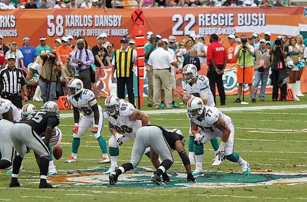 Jogadores dos Miami Dolphins de uniformes brancos e dos Oakland Raiders de verde, posicionados para o início da partida.