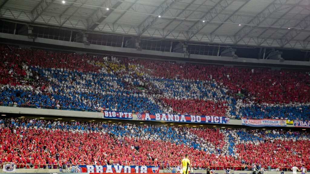 Arquibancada de estádio de futebol, lotada com torcida do Fortaleza vestindo vermelho e azul.