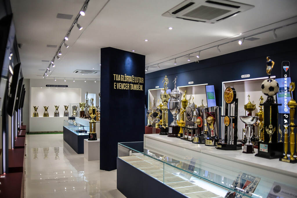 Sala de troféus do time do Fortaleza, com diferentes taças douradas espalhadas pelo ambiente.