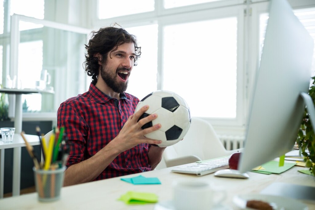 apostador comemora uma aposta acumulada vitoriosa, segurando uma bola de futebol na mao