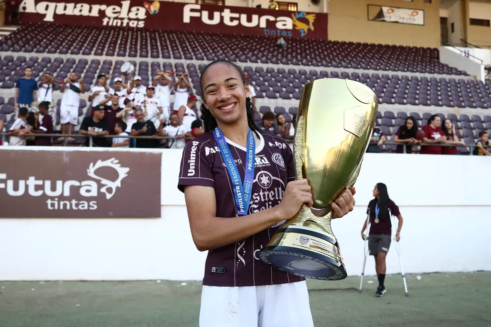 Jogadora de futebol com a taça de campeã em mãos 