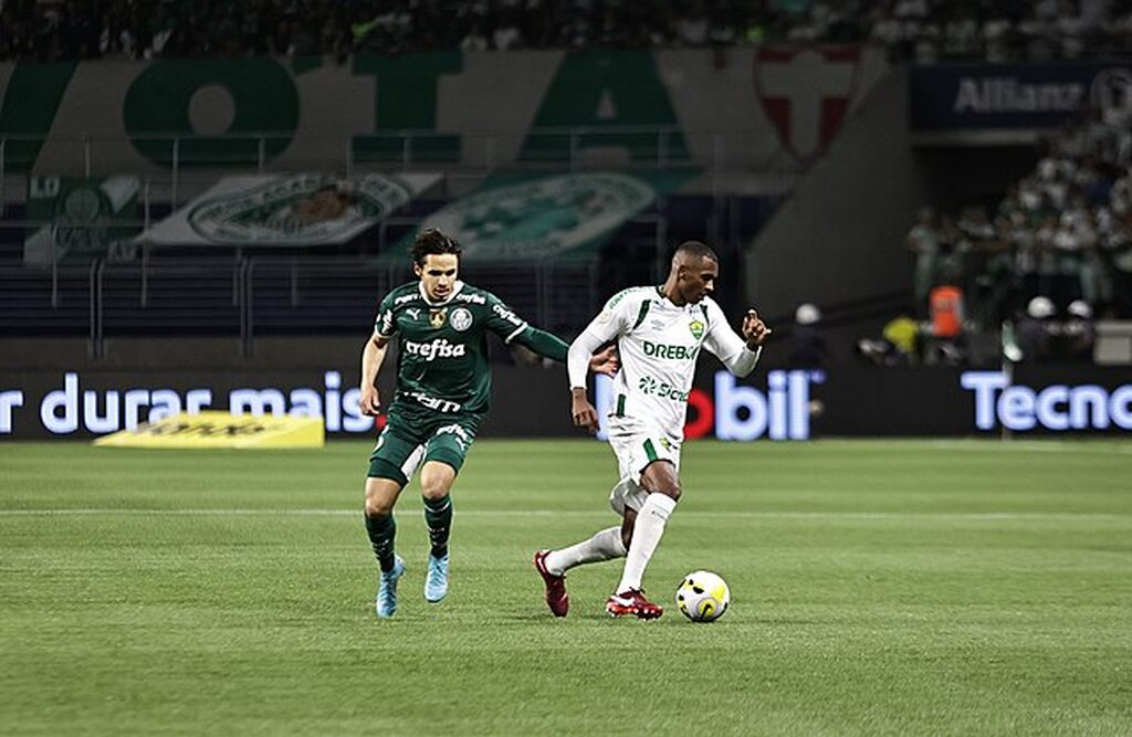 Jogador Raphael Veiga, do Palmeiras, disputando uma bola em campo contra um jogador do Cuiabá