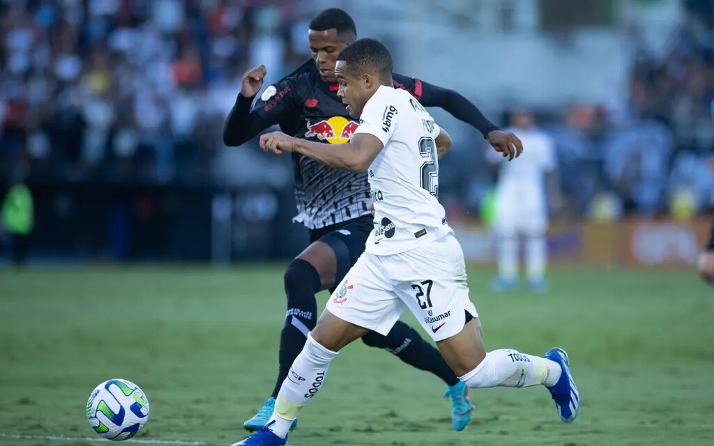 Imagem de dois jogadores, um do Corinthians e um do Bragantino, em campo e disputando uma bola de futebol