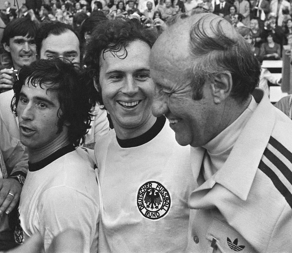 Franz Beckenbauer com o uniforme da seleção alemã, sorrindo e com outros colegas de time