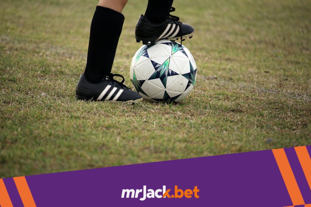 Jogador de futebol com chuteira e meião preto, com a bola dominada em baixo do pé.