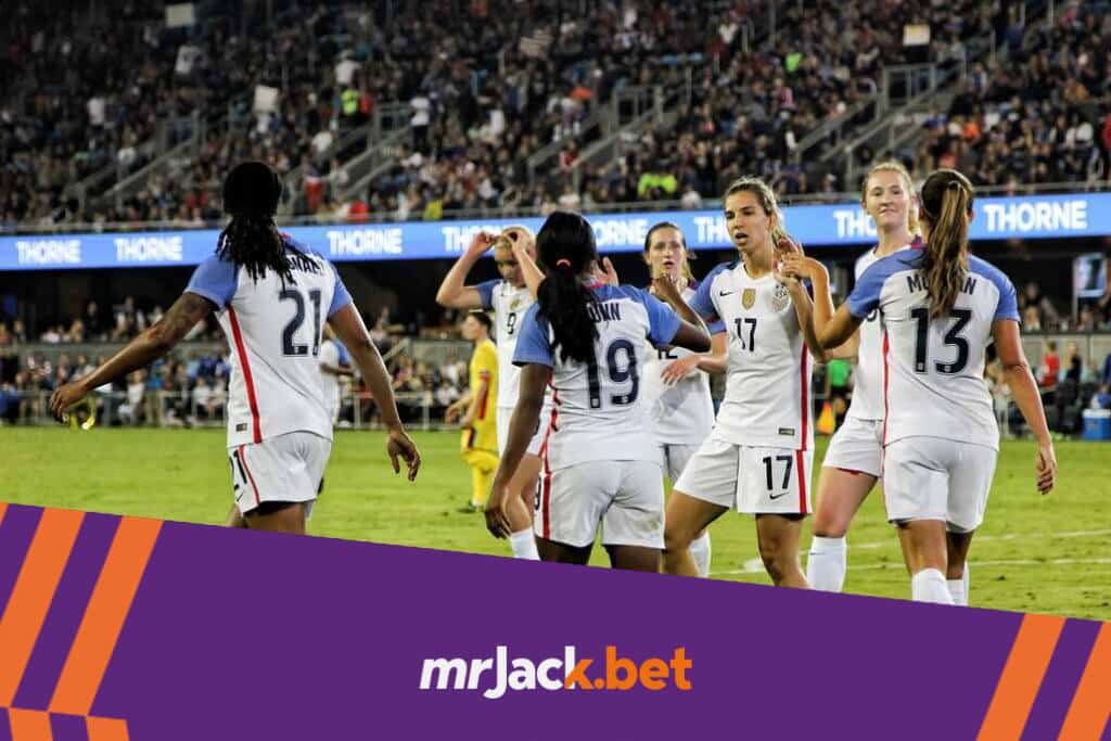 Jogadoras da saleção feminina vestindo um uniforme branco com detalhes azuis, e se cumprimentando em campo.