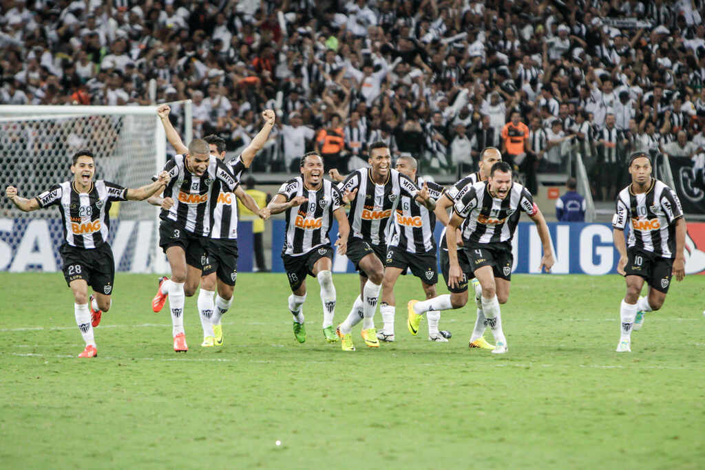 Jogadores de futebol do Atlético-MG, vestindo uniforme listrado, correndo pelo campo comemorando título da Libertadores.