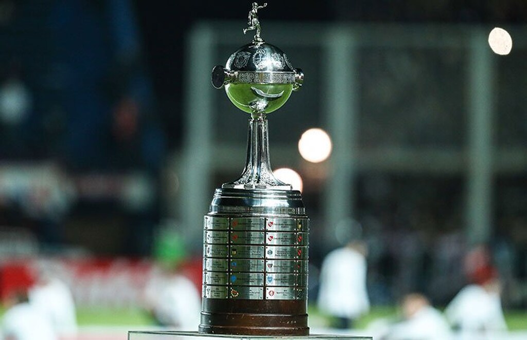 Taça da Copa Libertadores da América colocada em exposição no meio de um campo de futebol.