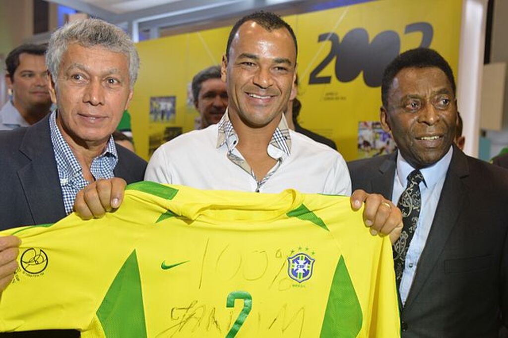 cafu, um dos capitaes da seleção brasileira, posado para a foto com pelé e outro homem, com a camisa da seleção erguida