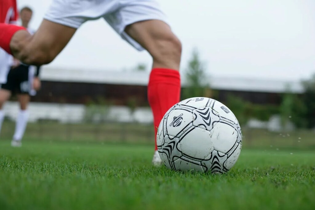 Jogador de futebol vestindo meião vermelho e calção branco realizando um chute com a perna direita.