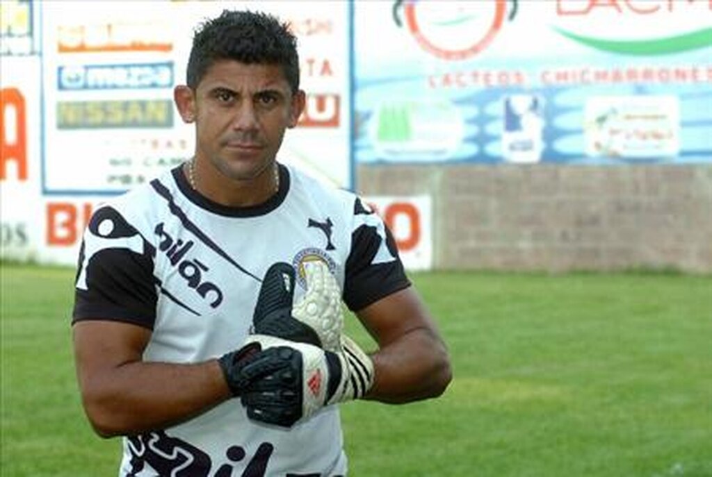 Jogador de futebol Misael Alfaro, usando luvas de goleiro, vestindo uniforme preto e branco enquanto olha para a câmera.