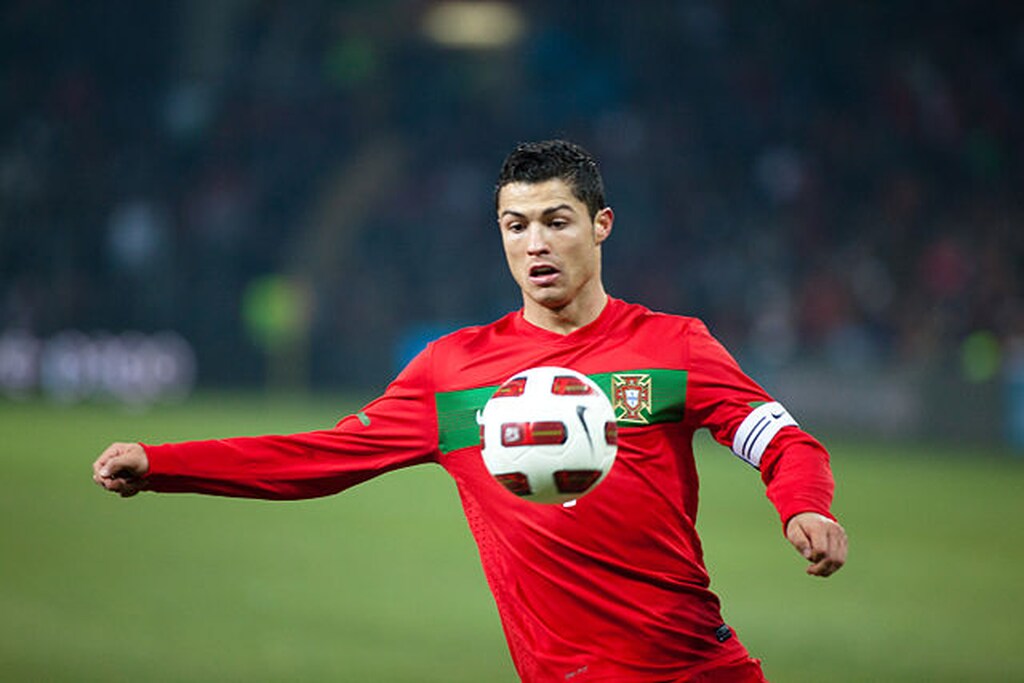 Jogador de futebol Cristiano Ronaldo de uniforme vermelho com listra verde da seleção de Portugal.