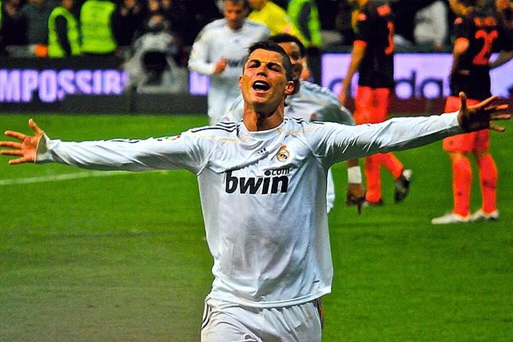 Jogador de futebol Cristiano Ronaldo comemorando gol com os braços abertos com a camisa do Real Madrid.