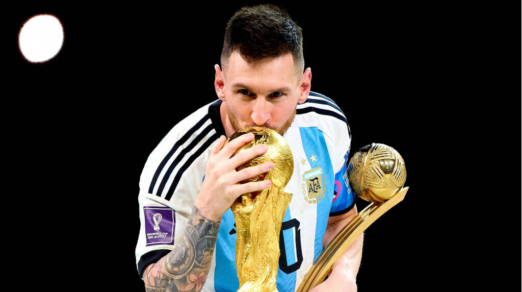 Lionel Messi beijando a taça da copa do mundo enquanto carrega a taça de melhor jogador da copa