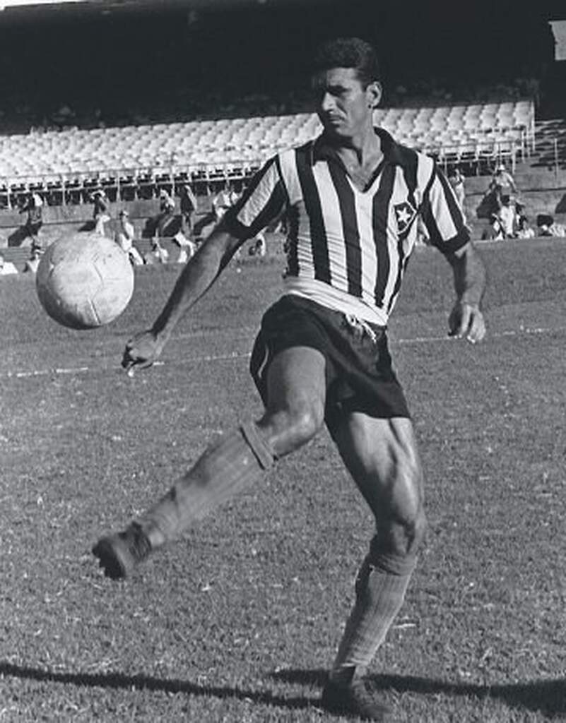 Ex-jogador de futebol do Botafogo, Nilton Santos, vestindo uniforme preto e branco e batendo embaixadinhas no campo.