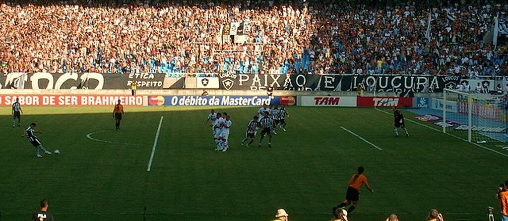 Visão da arquibancada de jogo do Botafogo durante cobrança de falta próxima do gol.