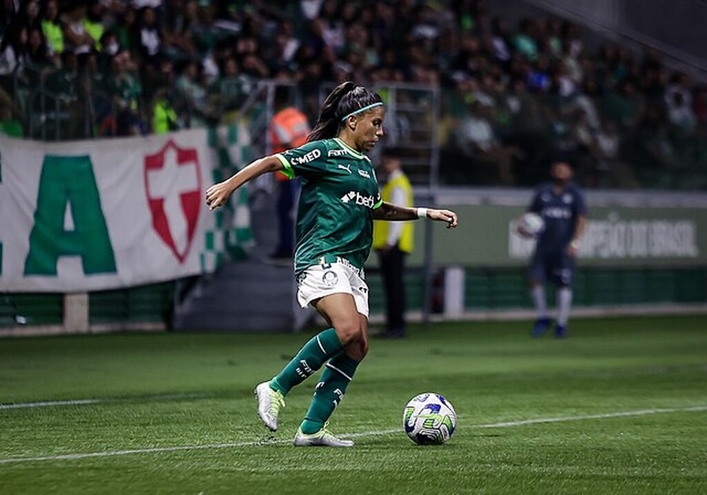 Jogadora de futebol do Palmeiras vestindo uniforme verde, dominando uma bola próxima da lateral durante partida.