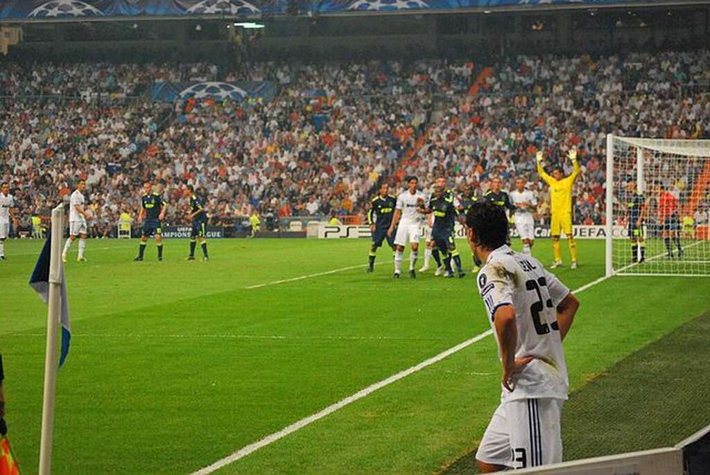 Jogador de futebol do Real Madrid, com as mãos na cintura, se preparando para realizar uma cobrança de escanteio.