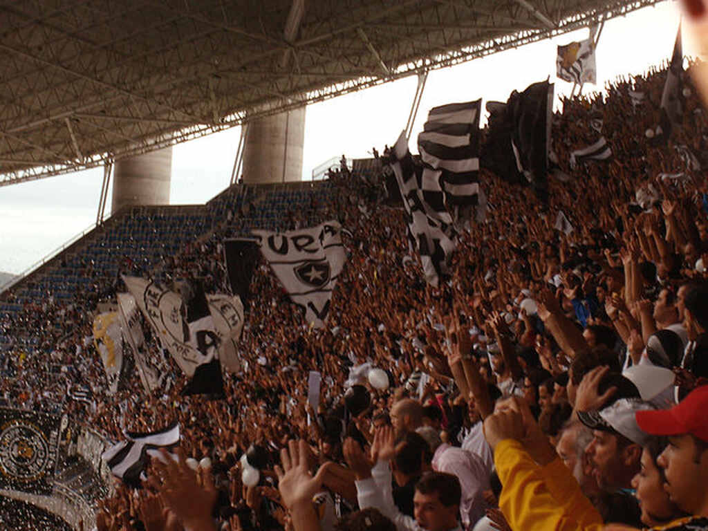 Torcida do Botafogo na parte mais alta da arquibancada assistindo e torcendo intensamente pelo time.