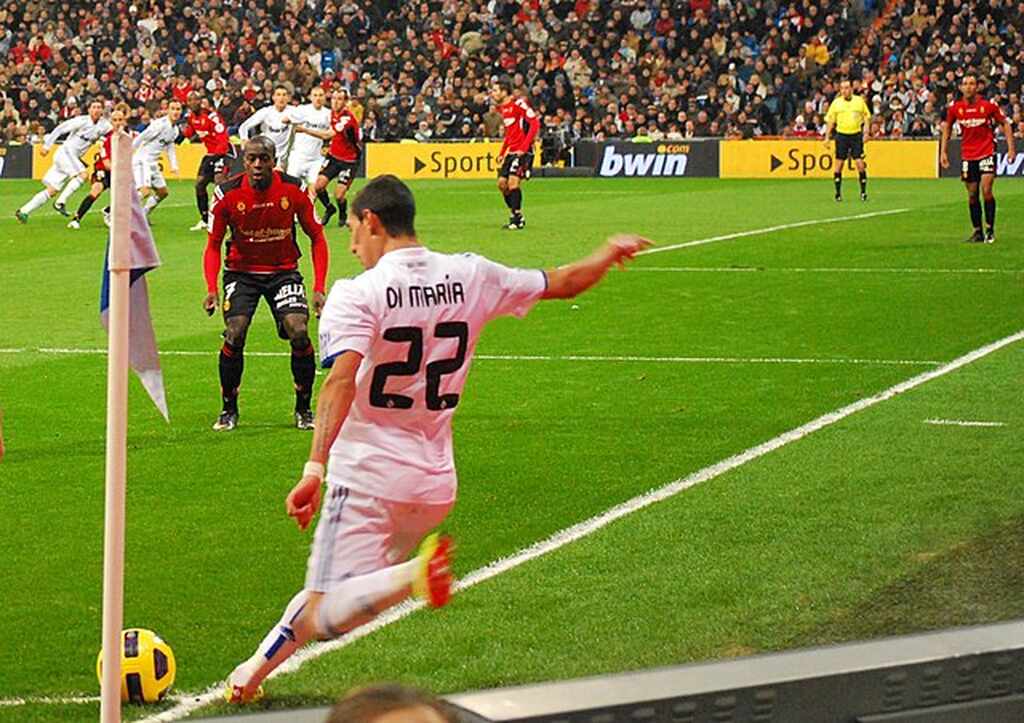 Jogador de Real Madrid, Di Maria, realizando uma cobrança de escanteio durante partida de futebol.