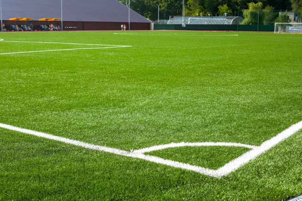 Marca de cobrnaça de escanteio, feita com linhas brancas em um campo de futebol com gramado verde.