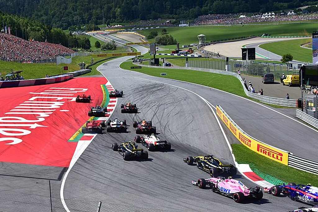 Sequência de carros de Fórmula 1, de diferentes cores, atravessando curva durante percurso da corrida.