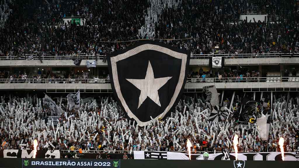 Torcida do Botafogo em estádio, erguendo o emblema doclube nas arquibancadas.