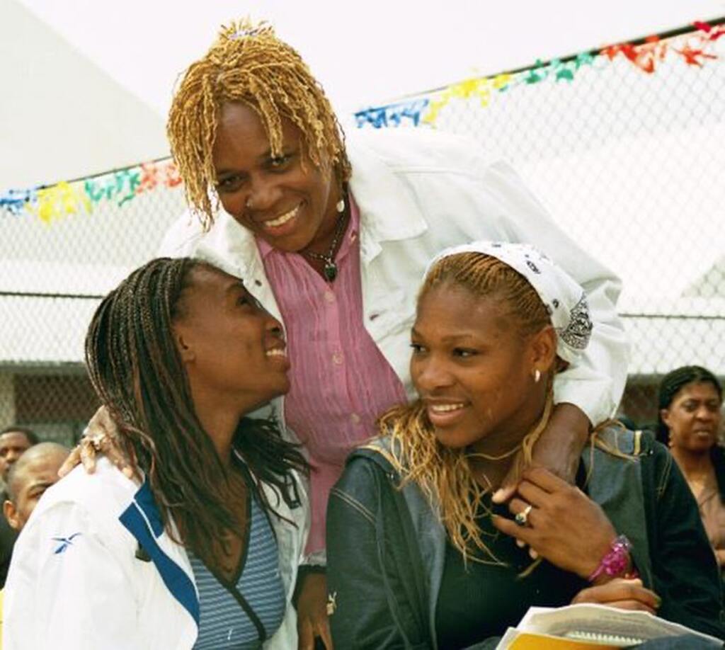 Ex-jogadora de tênis Serena Williams, junto com família em evento aberto, sorridente, de roupa rosa e casaco branco.