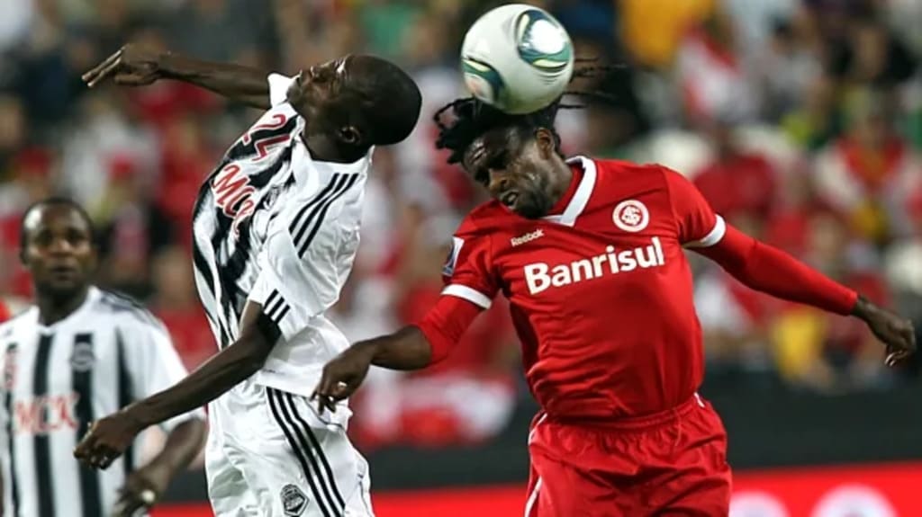 Jogador do Mazembe disputando a bola de cabeça com jogador do Internacional, durante partida do Mundial de Clubes.