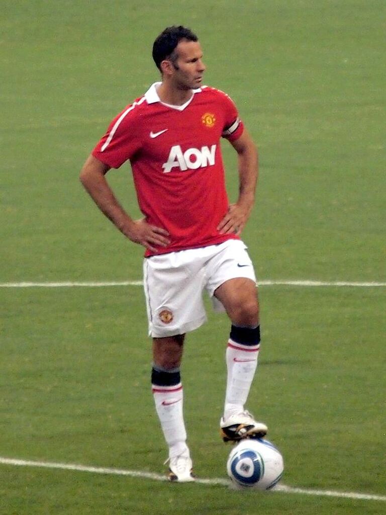 Ex-jogador de futebol, do Manchester United, vestindo uniforme vermelho do time, com a bola no pé, Ryan Giggs.