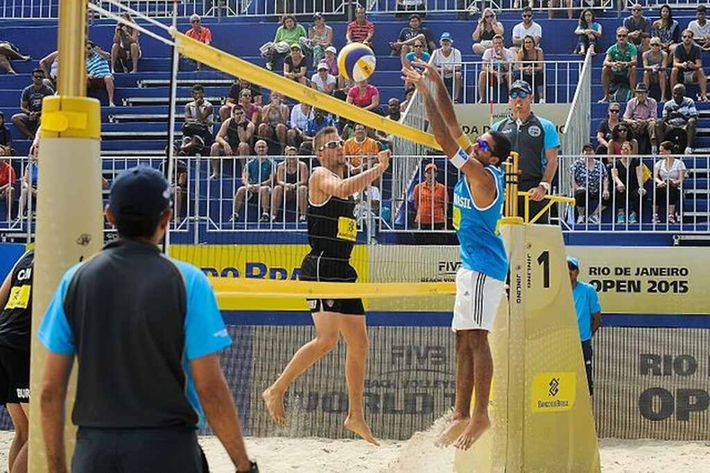 Jogador de vôlei de praia tentando evitar o ponto em bola cortada pelo jogador adversário, durante a partida.