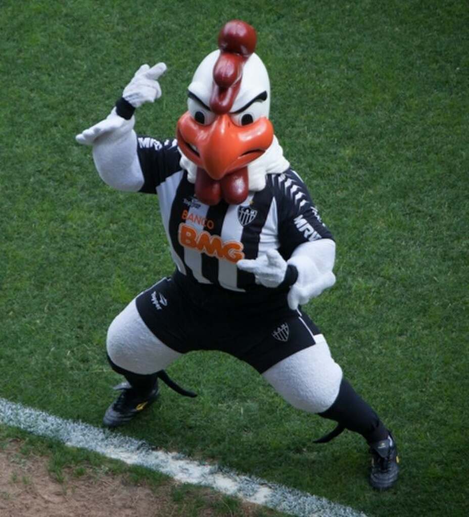 Mascote do Atlético-MG, o Galo, dançando próximo da linha lateral do campo de futebol.