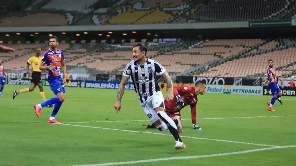 Jogador do Ceará, vestindo uniforme branco com listras pretas, comemorando gol em partida contra o Fortaleza.