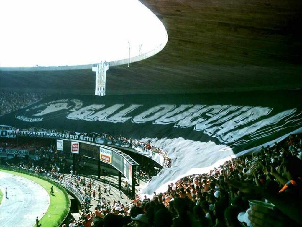 Torcida do Atlético-MG com uma bandeira estendida por toda a arquibancada durante partida de futebol.