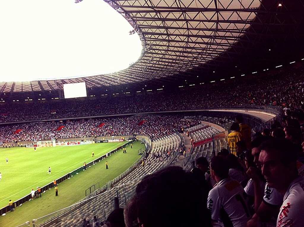 Torcida do Atlético-MG em estádio parcialmente cheio, durante partida de futebol, com vista para o campo.