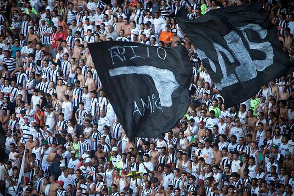 Torcida do Atlético-MG, vestindo uniforme listrado e erguendo bandeiras durante jogo de futebol.