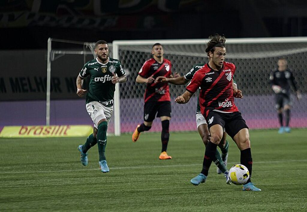 Jogador do Athlético PR com a bola dominada, tentando escapar da marcação do jogador do Palmeiras.