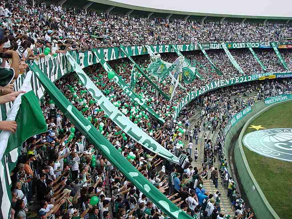 Arquibancada do estádio do Coritiba lotada, com torcida utilizando as cores do time, verde e branco.