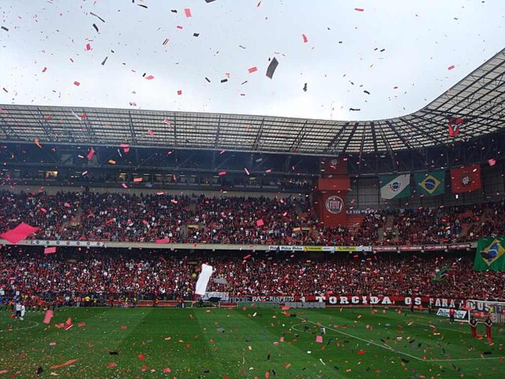 Festa da torcida do Athlético PR em estádio, com confetes com as cores do time sendo jogados das arquibancadas. 