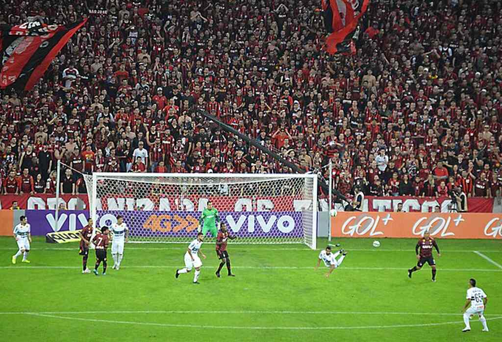 Partida de futebol do Coritiba, contra time de vermelho e preto, com vista para arquibancada lotada.