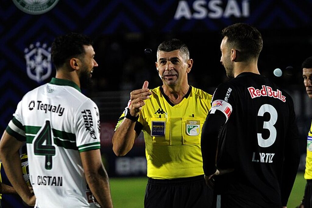 Capitão do Coritiba vestindo uniforme branco com detalhes verdes, conversando com árbitro antes do jogo.