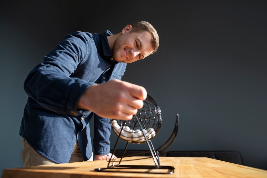 Homem de blusa azul de manga comprida, colocando bolinhas em um globo de metal sobre uma mesa de madeira.