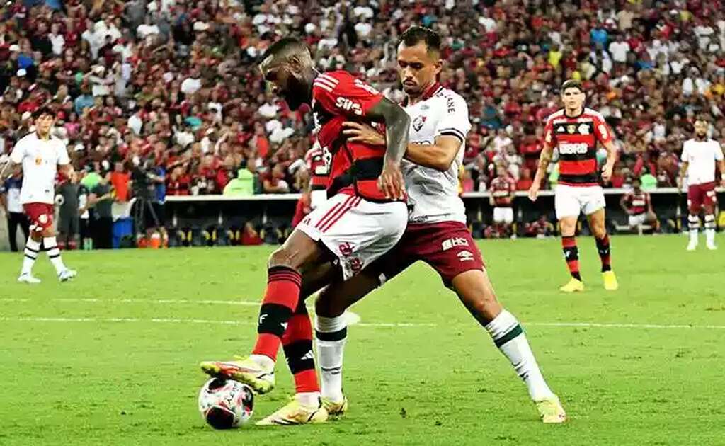 Jogador do Flamengo protegendo a bola enquanto jogador do Fluminense tenta recuperá-la.