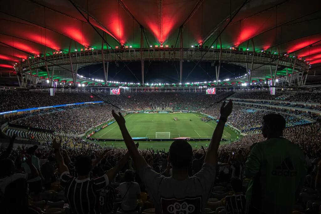 Estádio do Maracanã, lotado, com luzes com as cores do Fluminense sendo emitidas no teto.