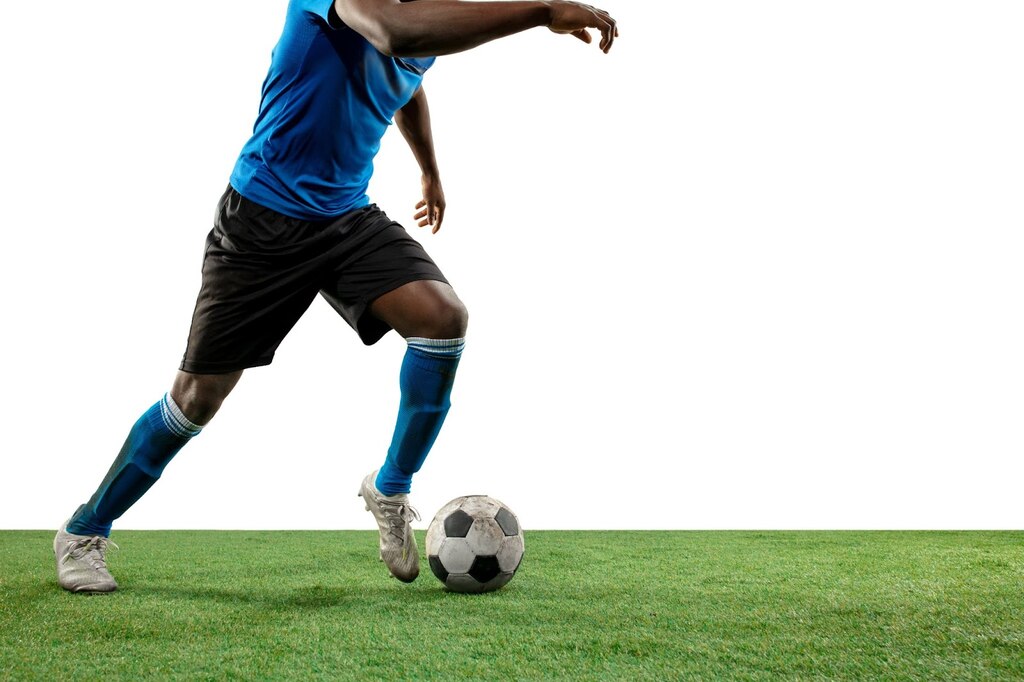 Jogador de futebol de uniforme azul e calção preto, conduzindo uma bola pelo gramado.