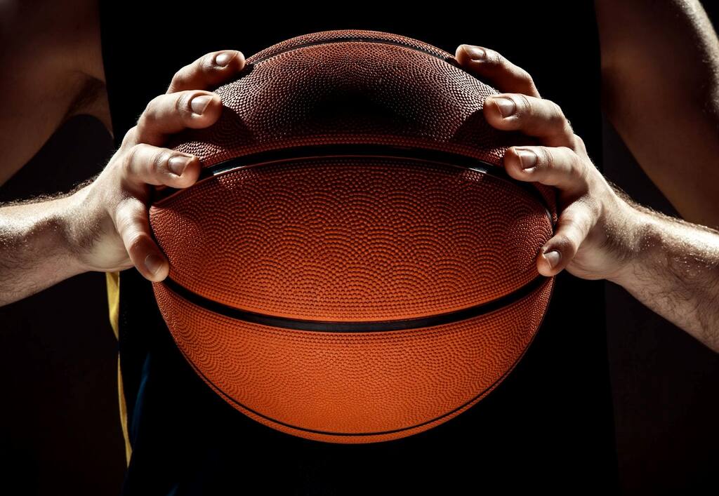 Jogador de basquete com regata preta e amarela, segurando uma bola com as duas mãos na frente de seu corpo.