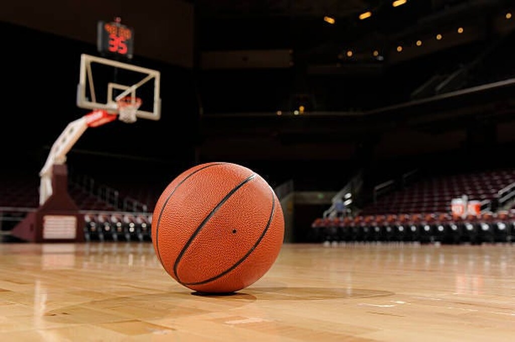 Bola de basquete com o logo da NBA no piso de uma quadra, com a tabela e a cesta ao fundo e as arquibancadas vazias.