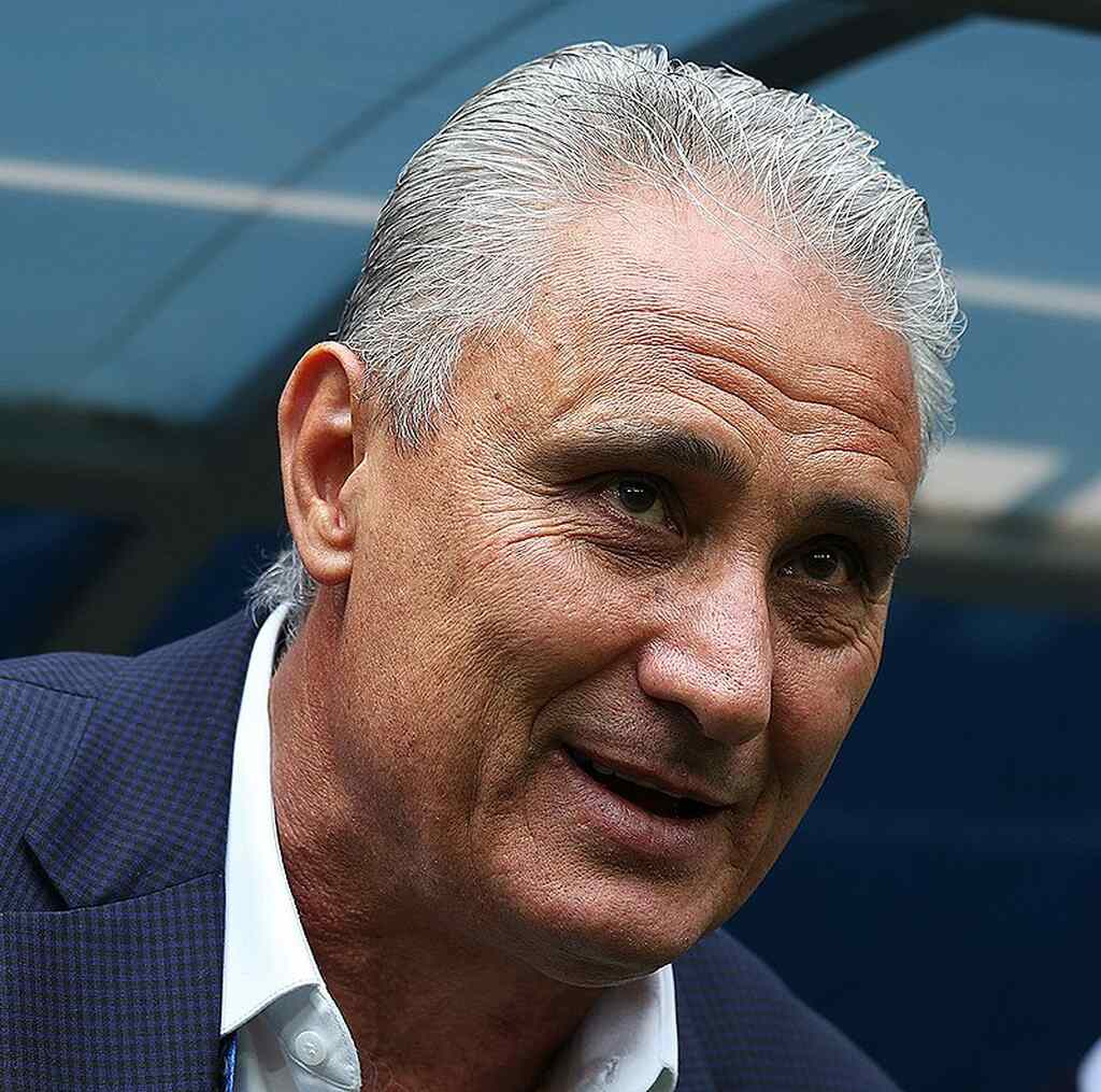 Tite, atual técnico do Flamengo, de paletó e camisa branca, esboçando sorriso na frente do banco de reservas durante partida