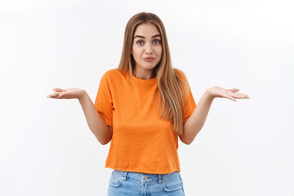 Mulher de camiseta laranja e calça jeans fazendo gesto e expressão de dúvida.